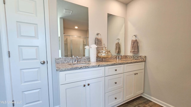 bathroom with double vanity, a shower stall, baseboards, and a sink