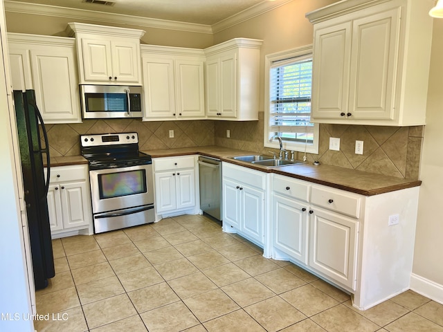 kitchen with light tile patterned floors, stainless steel appliances, crown molding, white cabinets, and sink