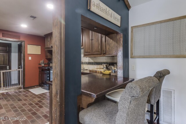 2213 N St, Gulfport, MS 39507 - kitchen with dark countertops, brick patterned floors, stove, a breakfast bar area, and recessed lighting