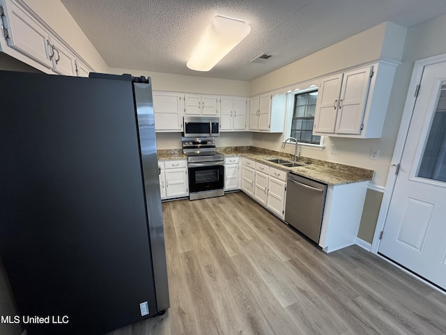 kitchen featuring visible vents, light wood-style flooring, appliances with stainless steel finishes, white cabinetry, and a sink