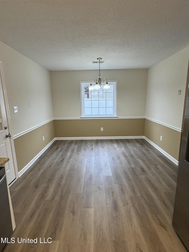 unfurnished dining area featuring a textured ceiling, dark wood-type flooring, visible vents, and a notable chandelier