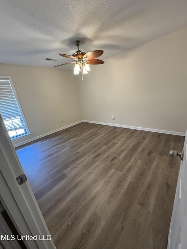 empty room with visible vents, baseboards, a ceiling fan, dark wood-style flooring, and a textured ceiling