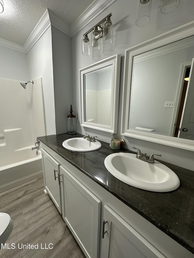 bathroom featuring bathing tub / shower combination, crown molding, hardwood / wood-style floors, a textured ceiling, and vanity