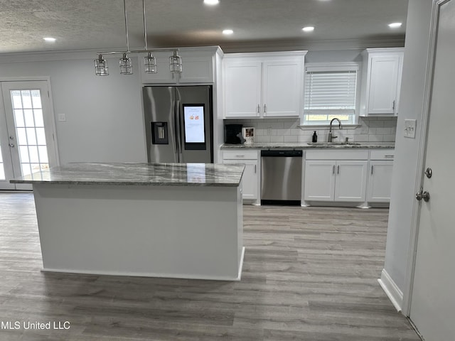 kitchen with pendant lighting, backsplash, white cabinets, sink, and stainless steel appliances