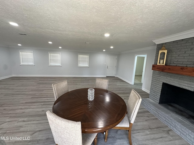 unfurnished dining area with wood-type flooring, ornamental molding, a textured ceiling, and a brick fireplace