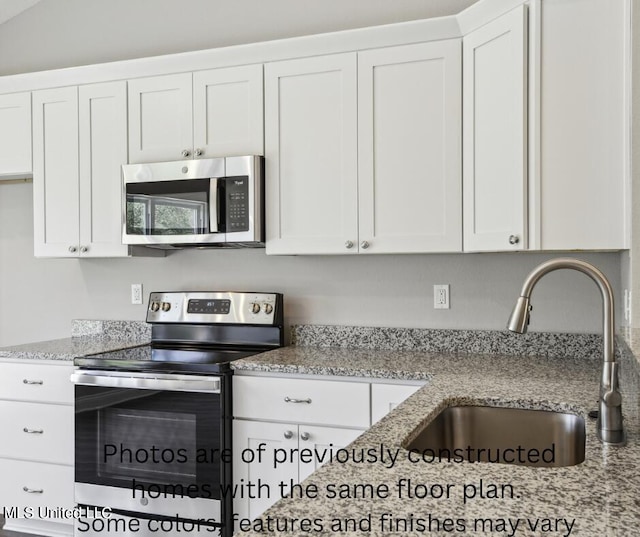 kitchen with lofted ceiling, white cabinets, light stone counters, appliances with stainless steel finishes, and sink