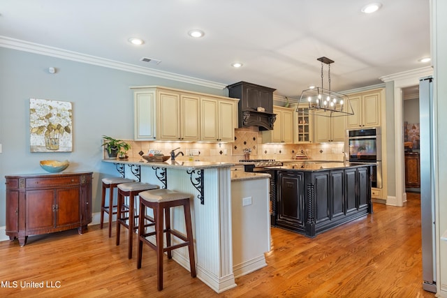 kitchen featuring cream cabinets, light stone counters, light hardwood / wood-style floors, crown molding, and decorative light fixtures