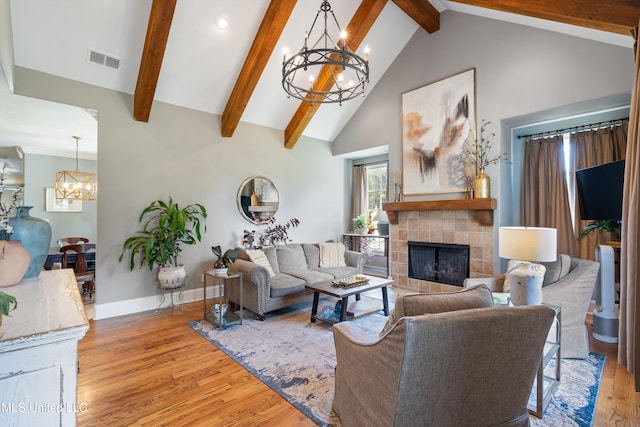 living room featuring beamed ceiling, a tile fireplace, an inviting chandelier, light wood-type flooring, and high vaulted ceiling