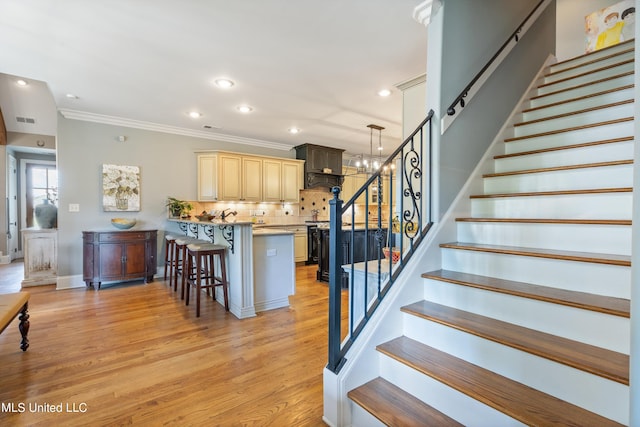 staircase featuring a notable chandelier, ornamental molding, and hardwood / wood-style floors