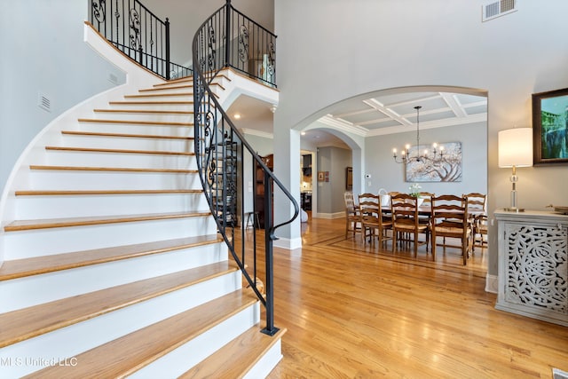 stairs with beam ceiling, hardwood / wood-style flooring, a chandelier, and coffered ceiling