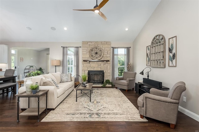 living area featuring healthy amount of natural light, ceiling fan, a stone fireplace, dark wood-style flooring, and high vaulted ceiling