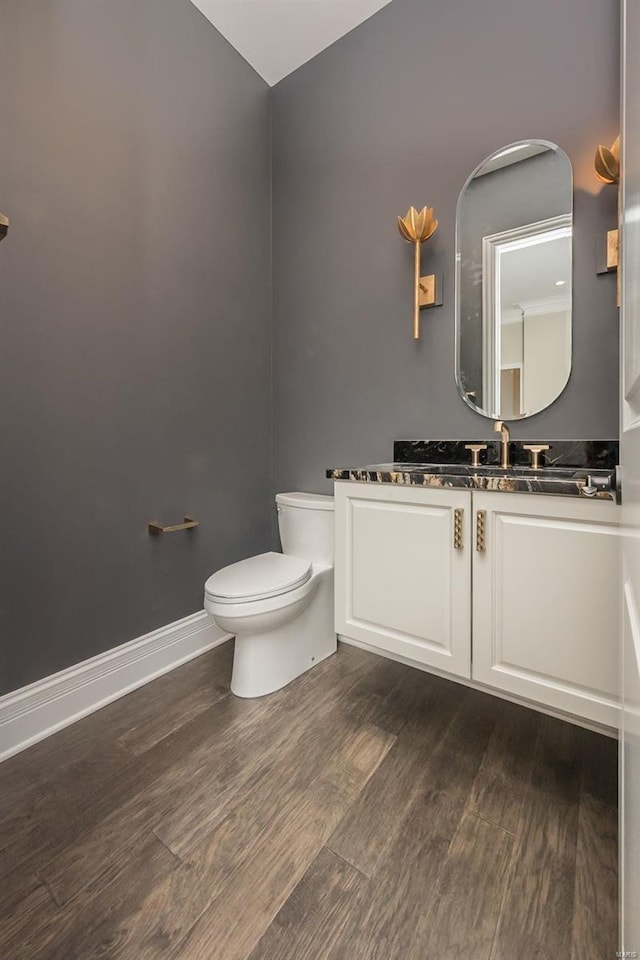 bathroom with wood finished floors, toilet, vanity, vaulted ceiling, and baseboards