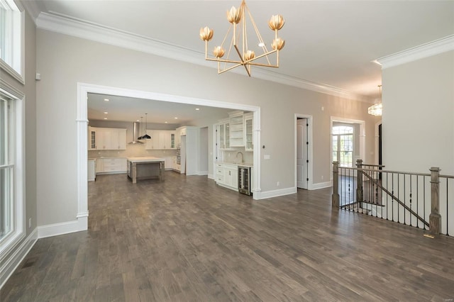 unfurnished living room featuring beverage cooler, a chandelier, crown molding, dark wood finished floors, and baseboards