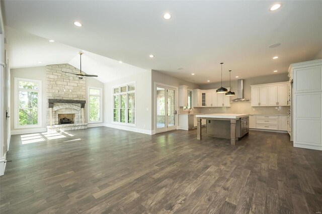 unfurnished living room featuring plenty of natural light, ceiling fan, dark wood-type flooring, a stone fireplace, and lofted ceiling
