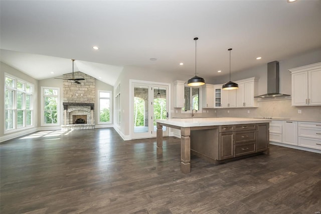 kitchen with wall chimney range hood, white cabinets, light countertops, dark wood finished floors, and lofted ceiling