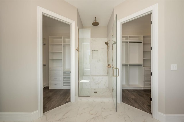 bathroom with a marble finish shower, marble look tiles, a walk in closet, and baseboards