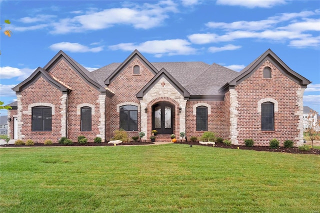 french country style house with brick siding, french doors, a front lawn, and a shingled roof