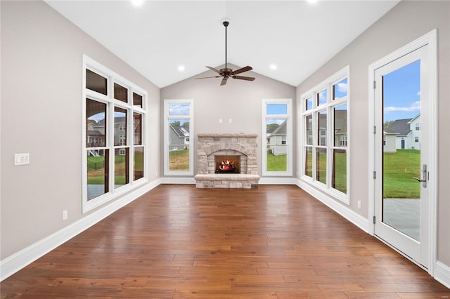 unfurnished living room with a stone fireplace, ceiling fan, healthy amount of natural light, lofted ceiling, and dark wood-type flooring