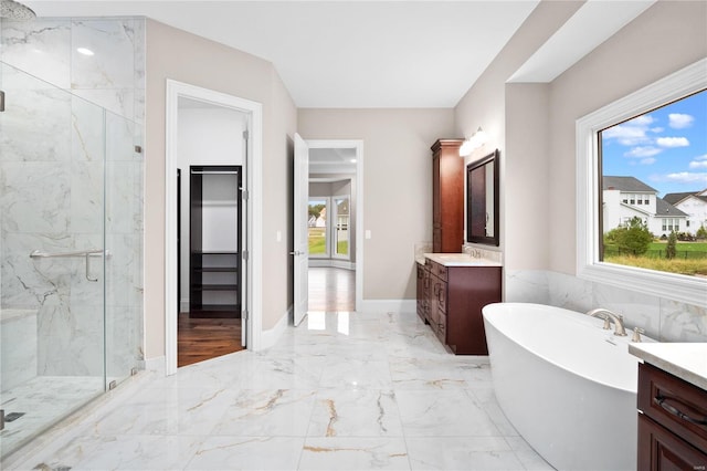 full bath with marble tiled floors, a marble finish shower, vanity, a freestanding tub, and a spacious closet