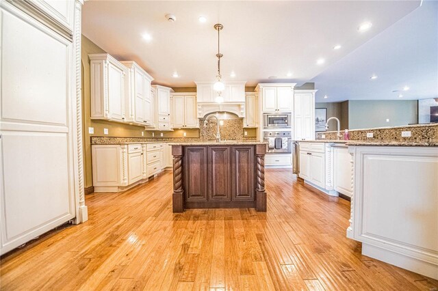 6708 Brown Ln, Poplar Bluff, MO 63901 - kitchen featuring appliances with stainless steel finishes, a spacious island, light wood finished floors, backsplash, and decorative light fixtures