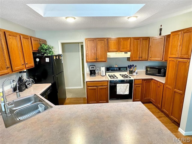 21 Forest Ln, Union, MO 63084 - kitchen with black appliances, under cabinet range hood, a sink, a skylight, and brown cabinets