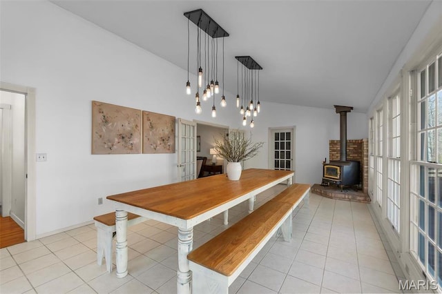 dining room featuring lofted ceiling, a wood stove, and light tile patterned flooring