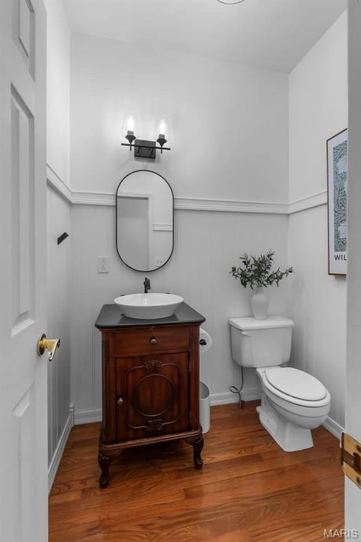 half bathroom with toilet, vanity, and wood finished floors