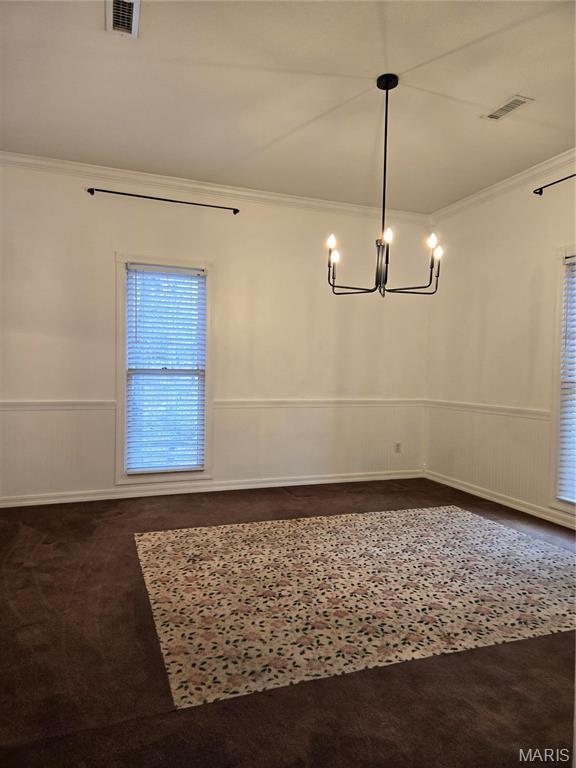unfurnished dining area featuring ornamental molding, a chandelier, dark carpet, and wainscoting