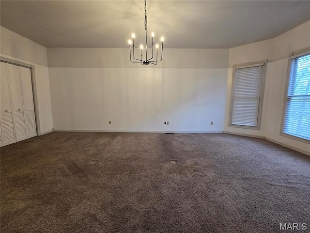 carpeted spare room featuring a chandelier and baseboards