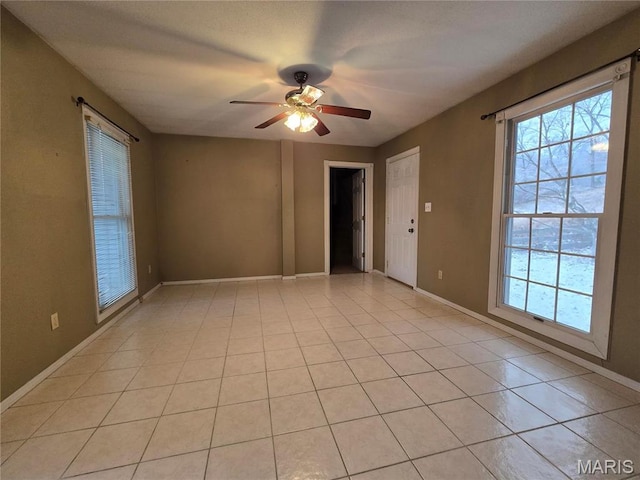 spare room featuring plenty of natural light, ceiling fan, light tile patterned flooring, and baseboards