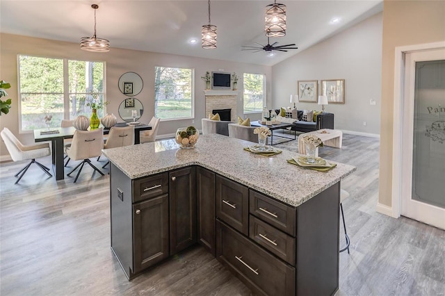 kitchen with a stone fireplace, hanging light fixtures, wood finished floors, baseboards, and lofted ceiling