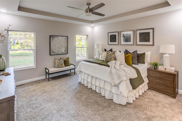 bedroom with a tray ceiling, light colored carpet, baseboards, and a ceiling fan