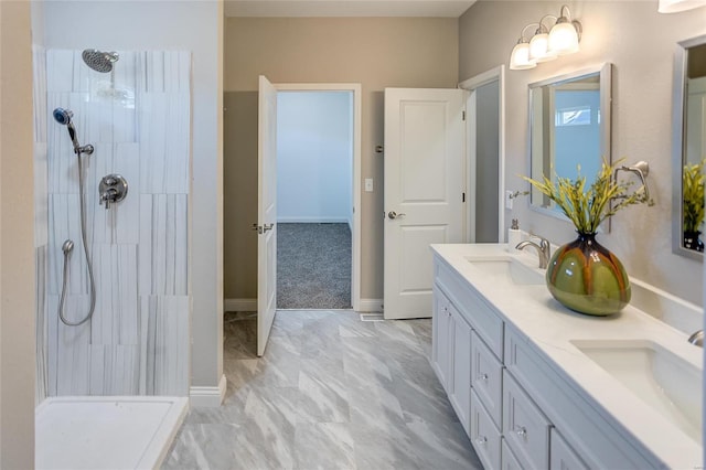 full bathroom featuring tiled shower, double vanity, marble finish flooring, and baseboards