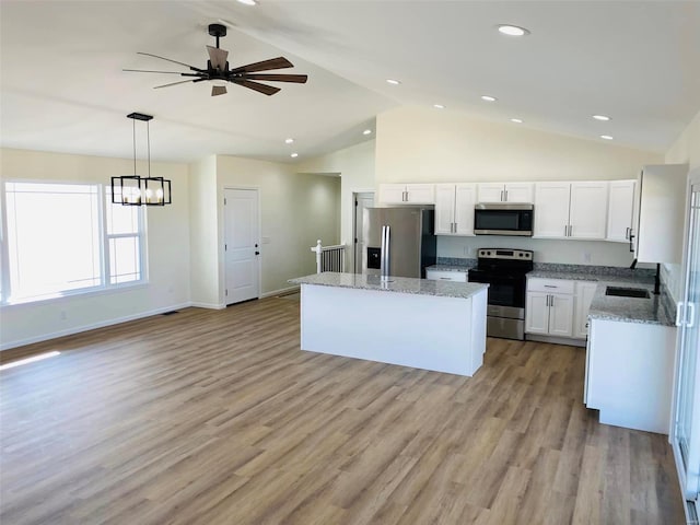 kitchen with appliances with stainless steel finishes, a center island, white cabinets, light stone countertops, and high vaulted ceiling