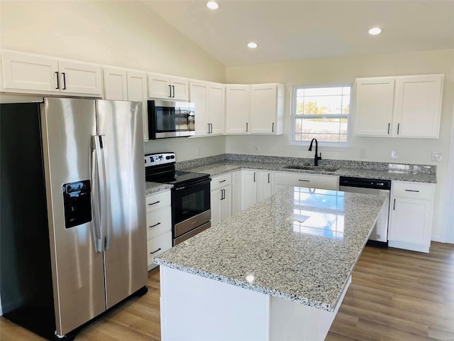 kitchen featuring stainless steel appliances, a sink, a center island, white cabinetry, and vaulted ceiling