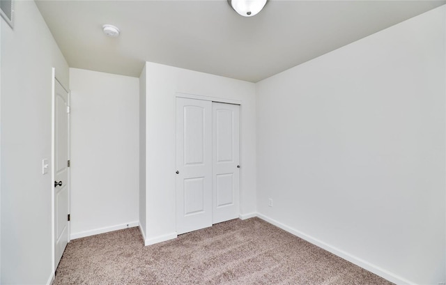 unfurnished bedroom with light colored carpet, a closet, and baseboards