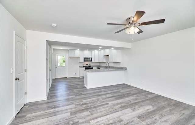 kitchen featuring appliances with stainless steel finishes, wood finished floors, white cabinetry, a peninsula, and baseboards