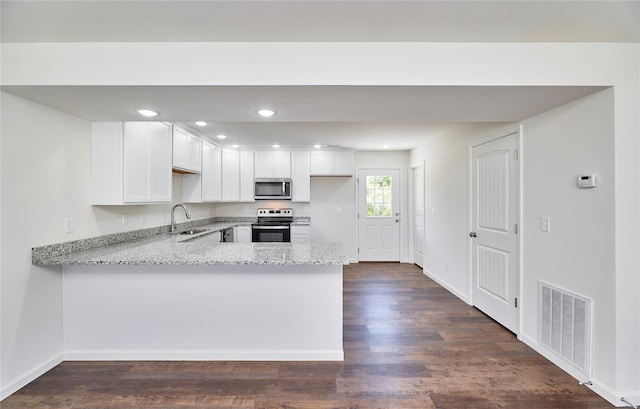 kitchen featuring stainless steel appliances, a sink, a peninsula, light stone countertops, and white cabinets