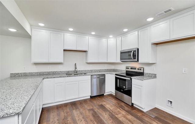 kitchen featuring appliances with stainless steel finishes, a sink, white cabinets, dark wood-style flooring, and recessed lighting