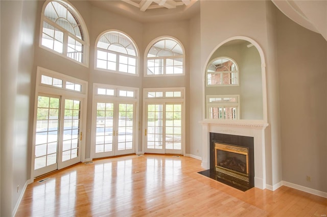 unfurnished living room with a towering ceiling, a fireplace with flush hearth, wood finished floors, and baseboards