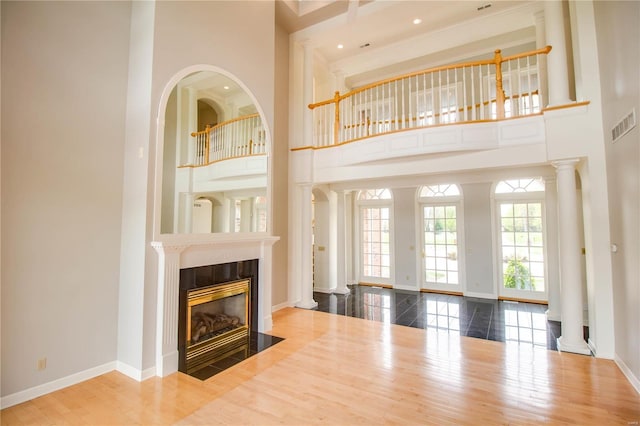 unfurnished living room featuring a towering ceiling, a fireplace, wood finished floors, baseboards, and decorative columns