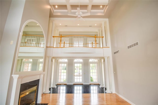 unfurnished living room featuring a towering ceiling, ceiling fan, beamed ceiling, a glass covered fireplace, and crown molding