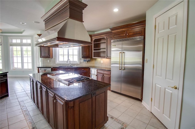 kitchen with stainless steel appliances, custom exhaust hood, tasteful backsplash, open shelves, and a center island