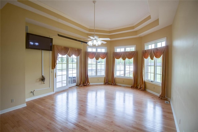 empty room with a ceiling fan, baseboards, light wood finished floors, crown molding, and a tray ceiling