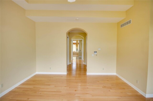 unfurnished room with arched walkways, light wood-style floors, and baseboards