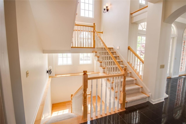 stairway with a towering ceiling, healthy amount of natural light, granite tiled floors, baseboards, and arched walkways
