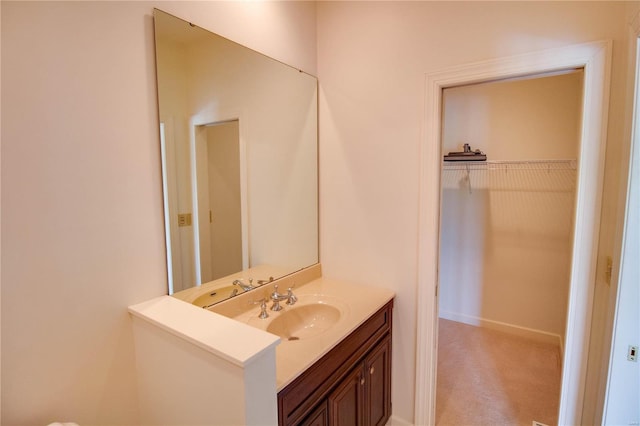 bathroom with vanity, a walk in closet, and baseboards