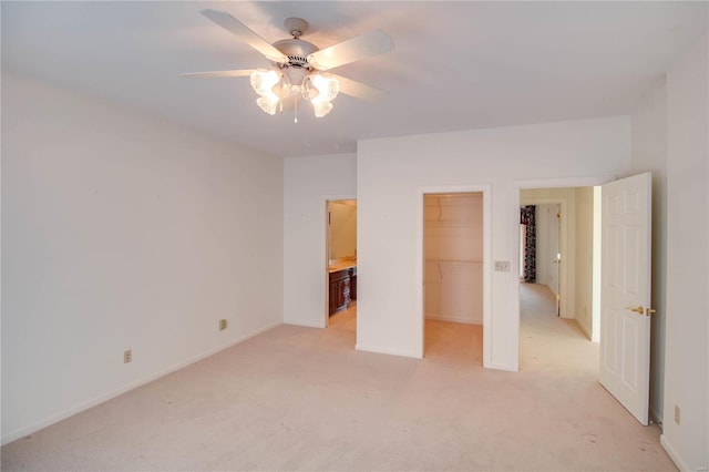 unfurnished bedroom featuring light carpet, a closet, baseboards, a walk in closet, and a ceiling fan