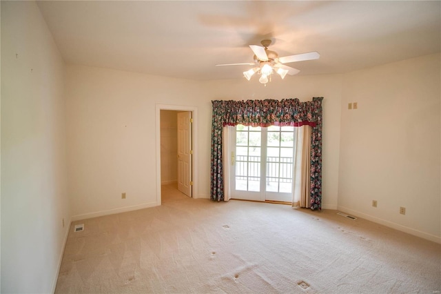 spare room featuring light carpet, a ceiling fan, and baseboards