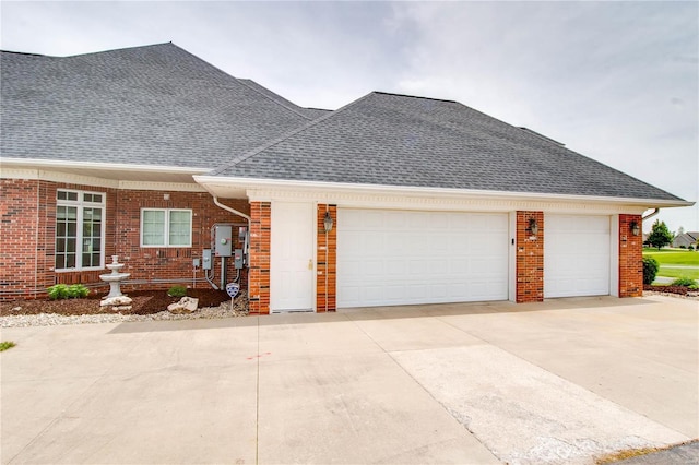 view of front of home with driveway, a garage, roof with shingles, and brick siding